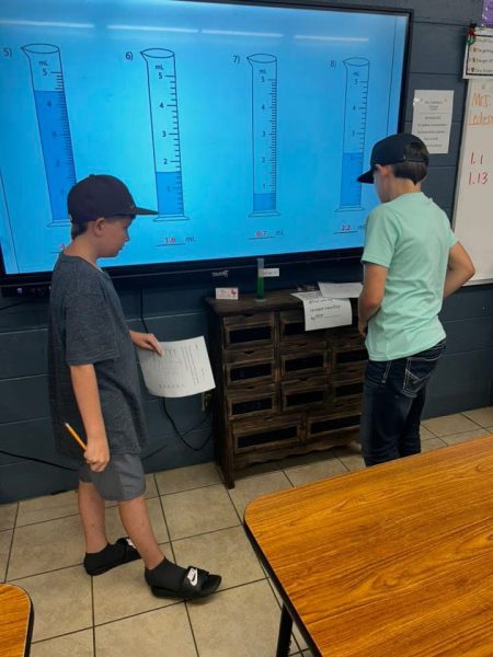 Young students working in a science lab with beaker diagrams on large monitor